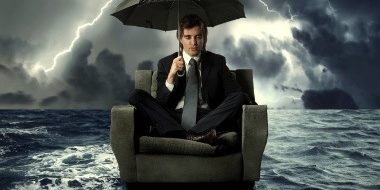 man sitting in chair holding umbrella over water with storm in background